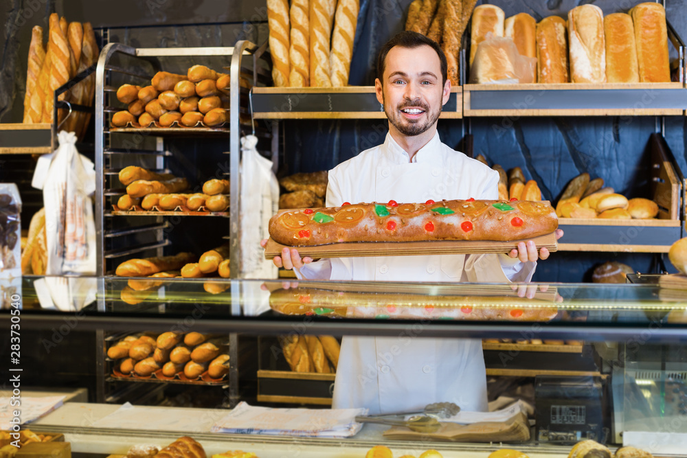 Man baker showing warm tasty bun in bakery