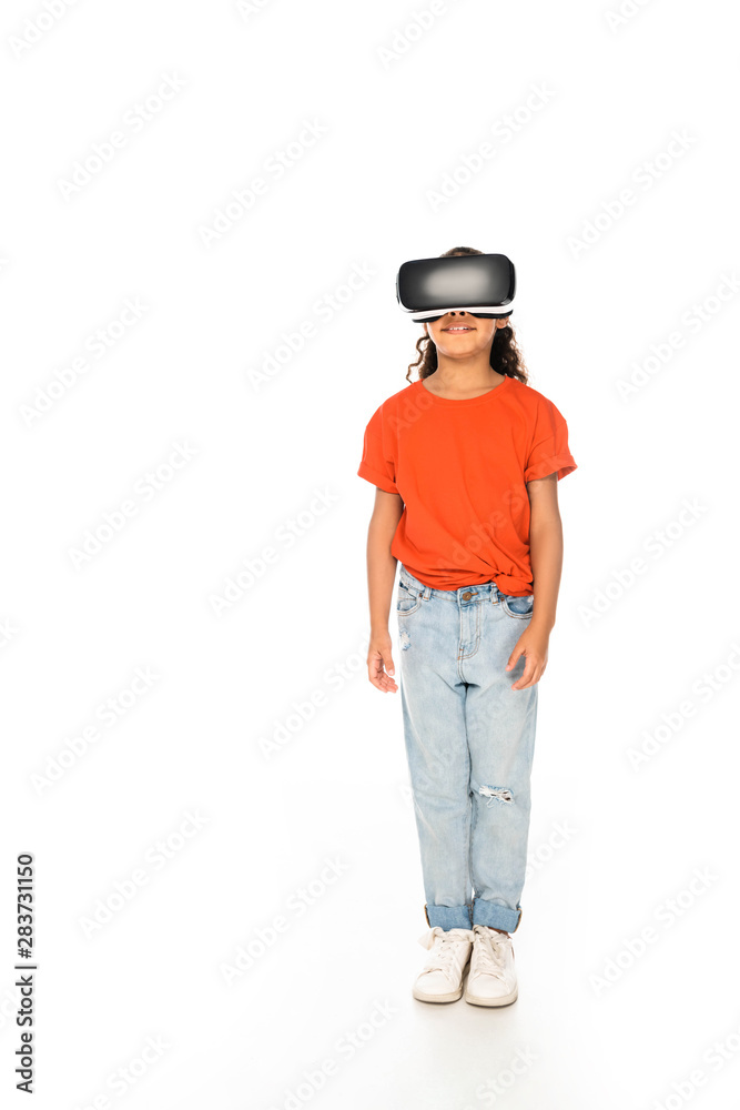 full length view of smiling african american kid using virtual reality headset on white background full length view of smiling african american kid using virtual reality headset on white background