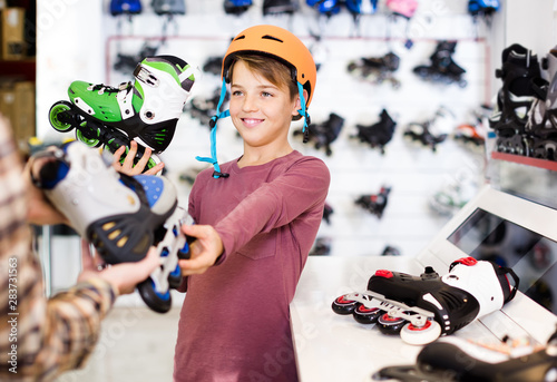Male shop assistant helping boy to choose roller-skates in sports store