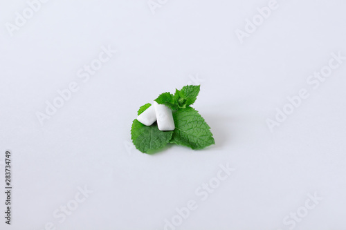 Close-up of the two pads of the chewing gum lies on the mint leaves on the light background.