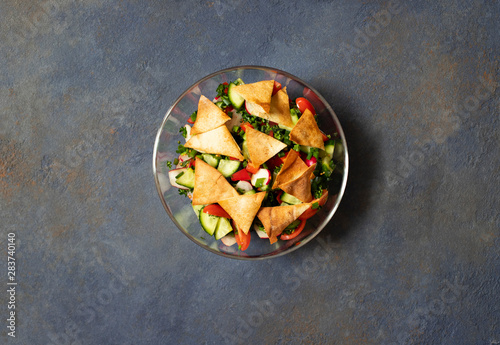 Traditional Fattoush salad  with vegetables and pita bread. Levantine, Arabic, Middle Eastern cuisine. Served in a glass plate with lemon, pita and olive oil. Dark background. Top view. Space for text