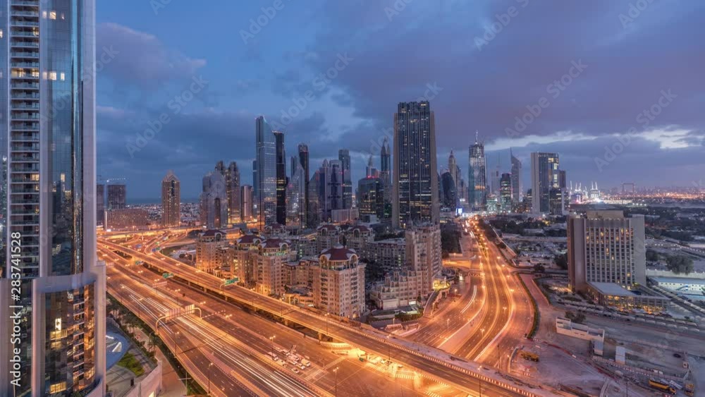Skyline view of the buildings of Sheikh Zayed Road and DIFC night to day transition timelapse in Dubai, UAE. Illuminated skyscrapers in financial centre aerial view from above in downtown