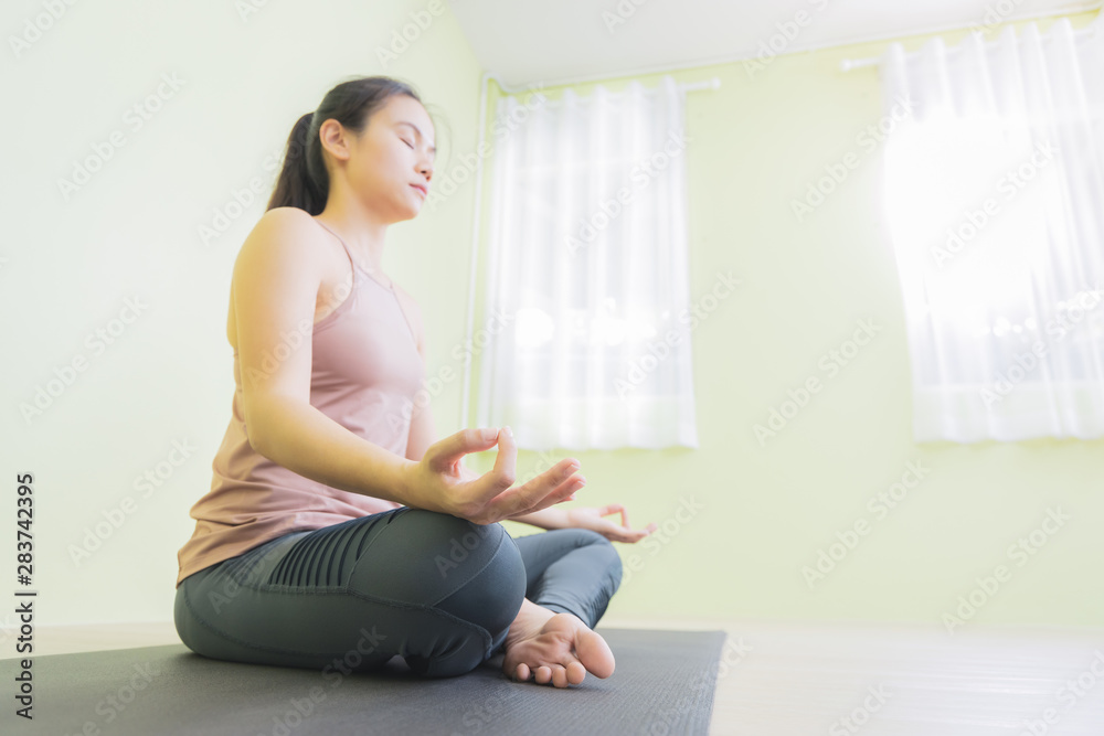 Asian woman sitting in lotus pose in yoga studio, low angle.