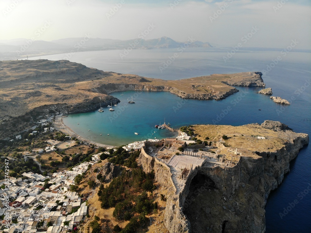 Lindos city view from air. Rhodes island. Sunny day. White houses and roofs. Castle and sea. Bay. 