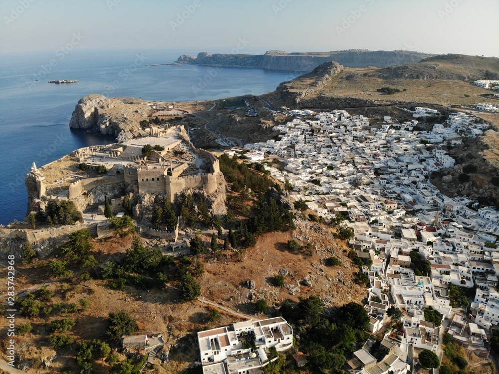 Lindos city view from air. Rhodes island. Sunny day. White houses and roofs. Castle and sea. Bay. 