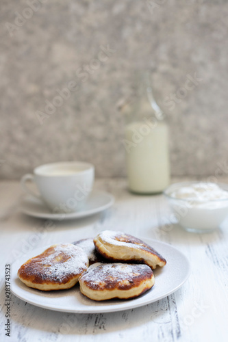 Cottage cheese pancakes, Cheesecakes on the table. Syrniki or sirniki. Healthy breakfast. White dishes. Bottle of milk. A cup of milk. Yogurt or sour cream. White background. Close up