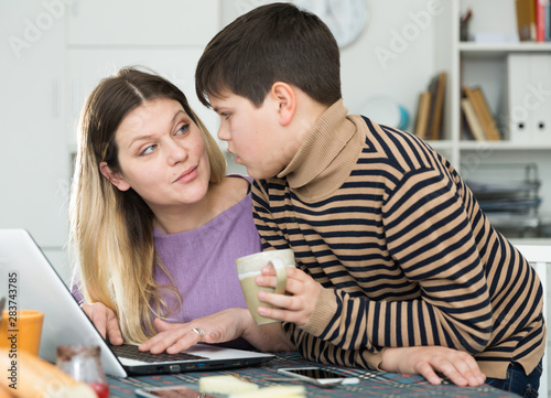 Portrait of young woman and son chatting at table with laptop