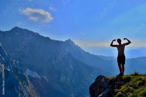 Young man is posing on the edge of rock. Beautiful mountains in background.