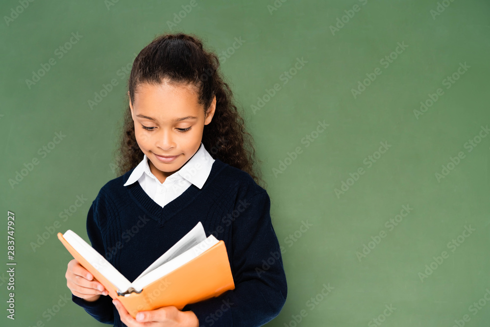 attentive african african american schoolgirl reading book while standing near chalkboard attentive african african american schoolgirl reading book while standing near chalkboard