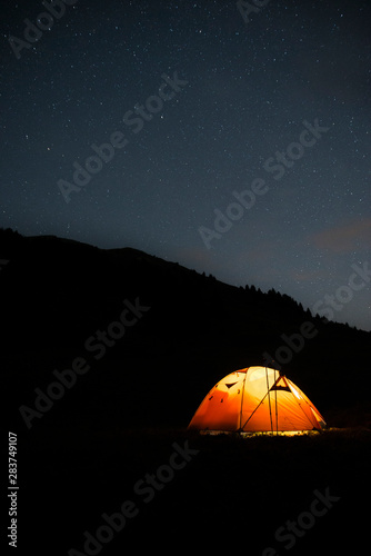 Silhouette of an illuminated trekking tent in high mountain during a starry night