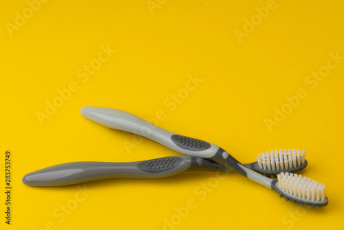 Two different grey  toothbrushes on a yellow background. All you need for teeth.