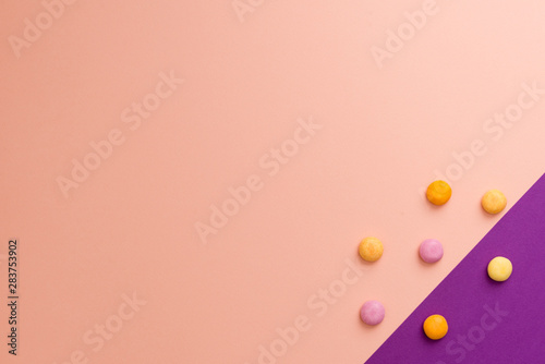 Round with multi-coloured candies on a coloured background. Pink and purple. 