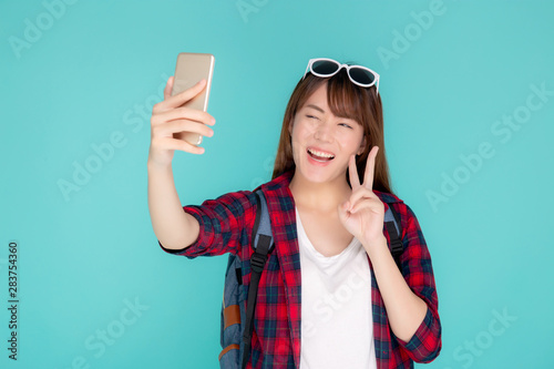 Beautiful portrait young asian woman cheerful smiling and take selfie on smart mobile phone, beauty girl wear travel summer enjoy and fun in vacation isolated on blue background, holiday concept.