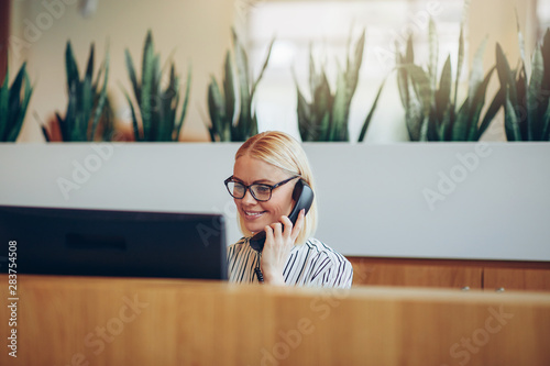 Smiling businesswoman talking on the telephone at a reception de Fototapet