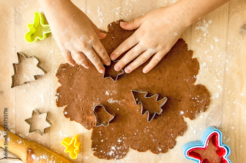 Faceless child preparing Christmas cookies From above crop kid cutting out fir tree shape from dough while cooking ginger biscuits at home