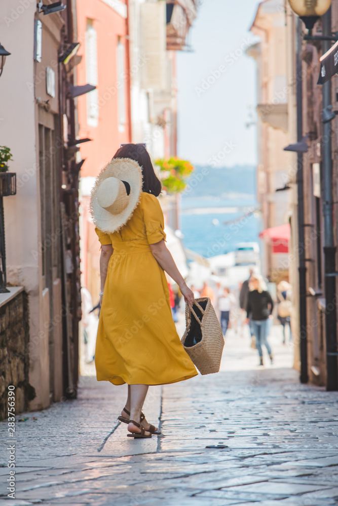 young pretty woman in yellow dress walking by small porec city streets sea on background