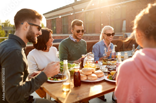 leisure and people concept - happy friends having dinner or barbecue party and eating on rooftop in summer