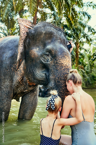 Mother and daughter washing an Asian elephant in a river