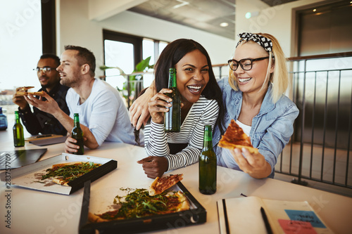 Two businesswomen laughing over pizza and beers after work