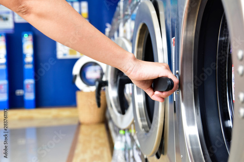 Women hand open side load washing machine in self service laundry room