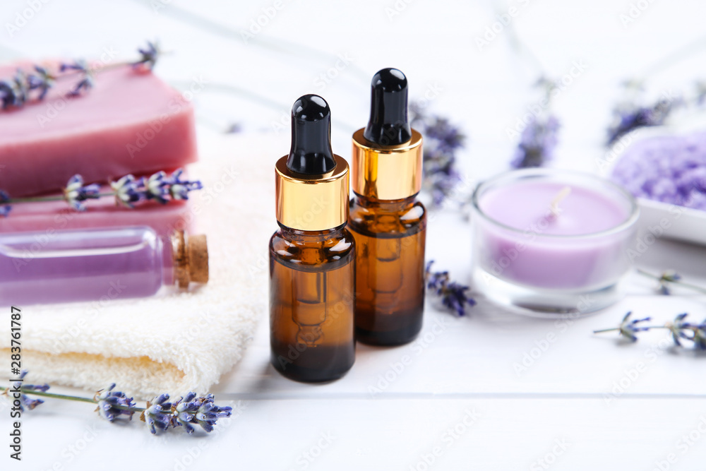 Lavender oil in bottles with flowers, candle and soap on white wooden table Lavender oil in bottles with flowers, candle and soap on white wooden table