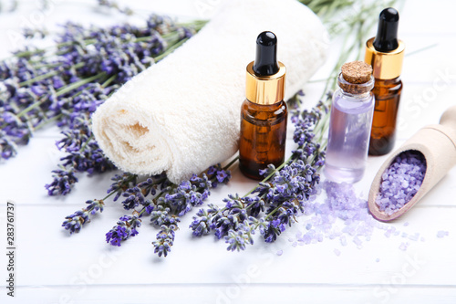 Lavender flowers with oil in bottles, salt and towel on white wooden table