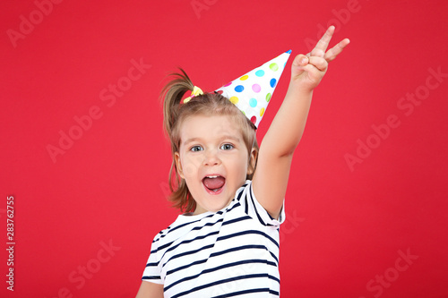 Cute little girl in birthday cap on red background