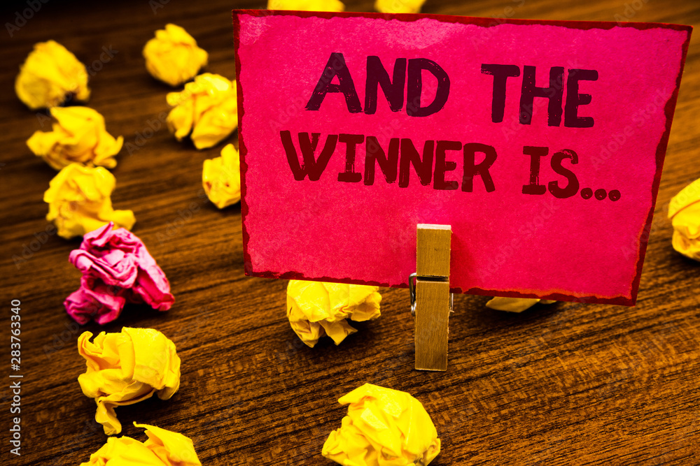 Fototapeta premium Conceptual hand writing showing And The Winner Is . Business photo showcasing Announcing as first place in competition or race Paperclip retrain pink card with letters wooden floor hunch