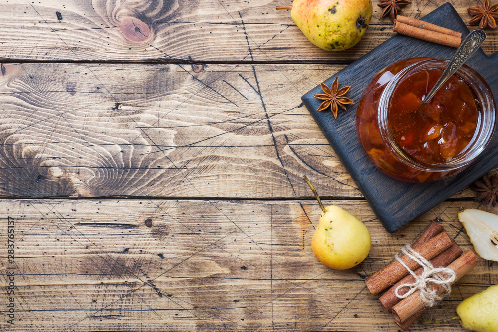 Homemade pear jam in a jar and fresh pears on a wooden background. Copy space.