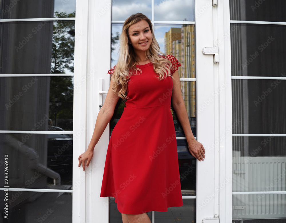 A young girl in a red dress stands on the background of Windows and doors. A young girl in a red dress stands on the background of Windows and doors.