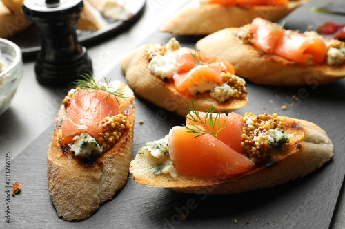 Tasty bruschettas with salmon and blue cheese on slate plate, closeup