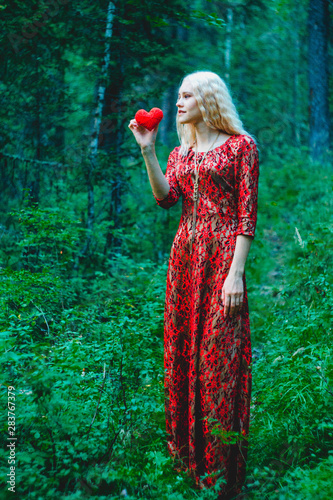 a blonde in a red dress in the woods with a red heart of thread in her handsa blonde in a red dress in the woods with a red heart of thread in her hands photo