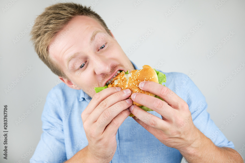 young handsome man biting tasty burger from fast food restaurant looks hungry on isolated white background young handsome man biting tasty burger from fast food restaurant looks hungry on isolated white background