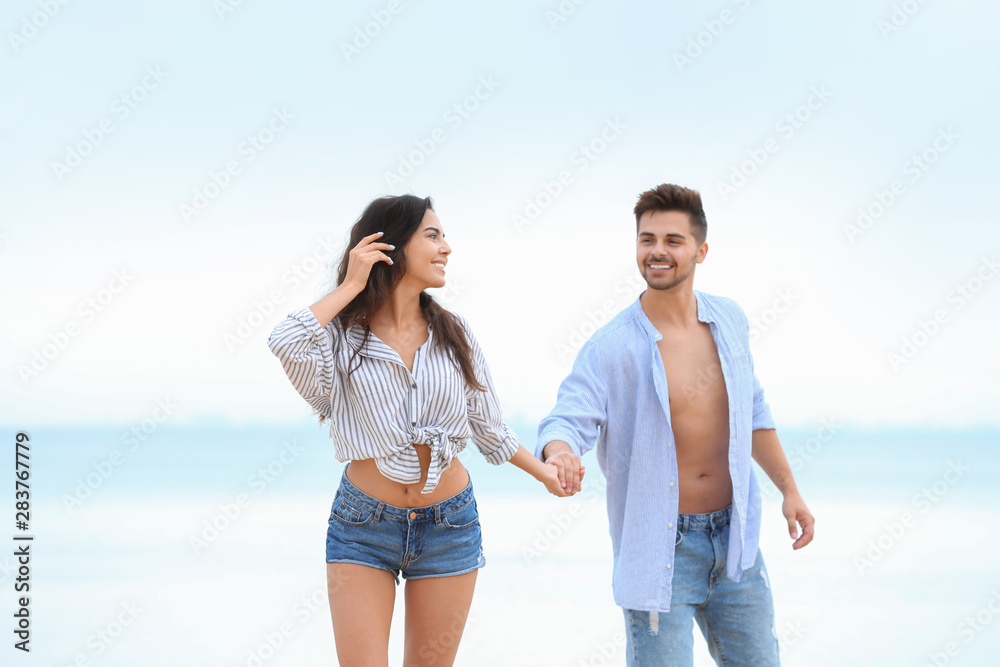 Happy young couple walking together on beach near sea Happy young couple walking together on beach near sea