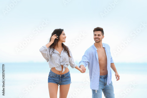 Happy young couple walking together on beach near sea