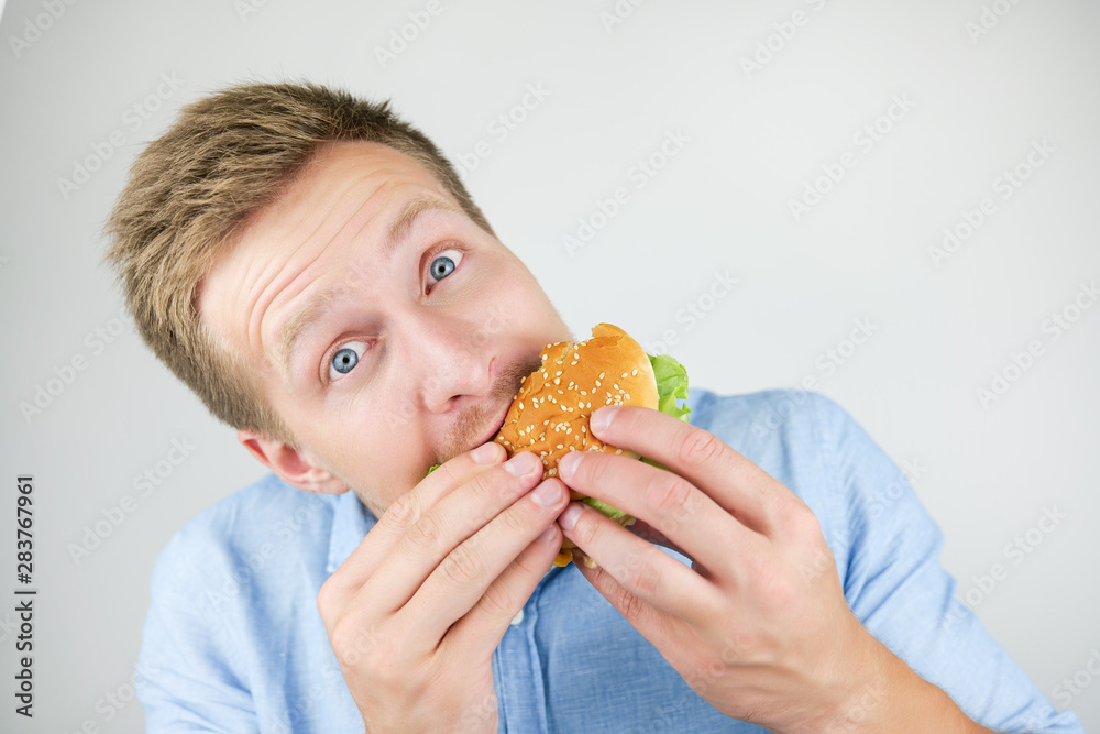 young handsome man eats fresh tasty burger from fast food restaurant looks hungry on isolated white background young handsome man eats fresh tasty burger from fast food restaurant looks hungry on isolated white background