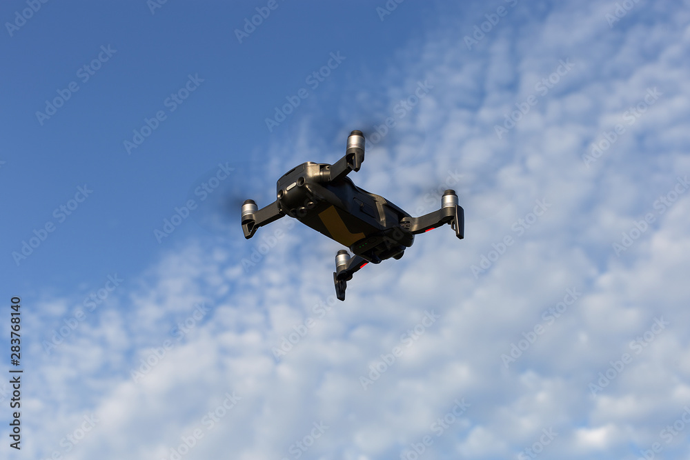 A drone, a quadrocopter with a camera for video shooting, flies against a blue sky with clouds. A drone, a quadrocopter with a camera for video shooting, flies against a blue sky with clouds.