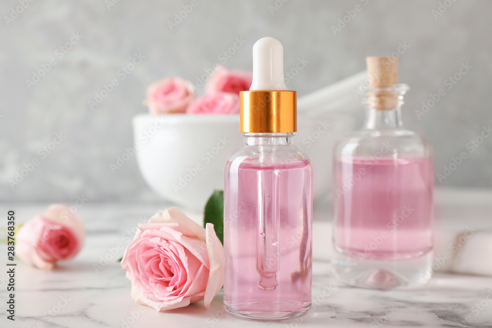 Bottle of essential oil and rose on marble table