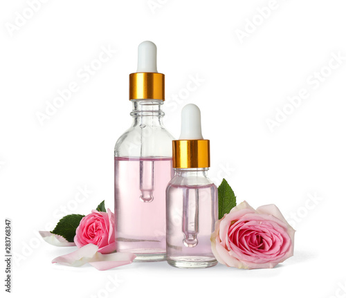 Bottles of essential oil and roses on white background