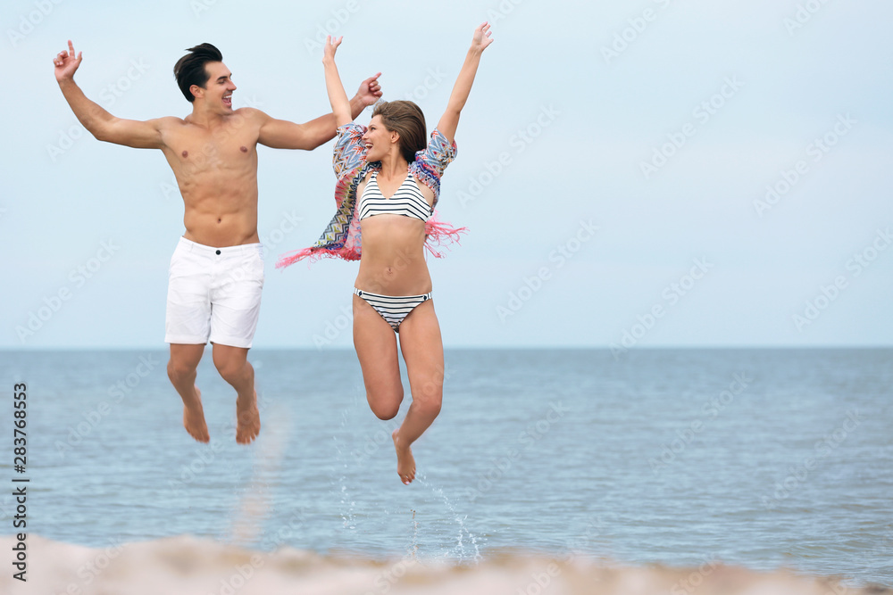 Happy young couple jumping together on sea beach. Space for text