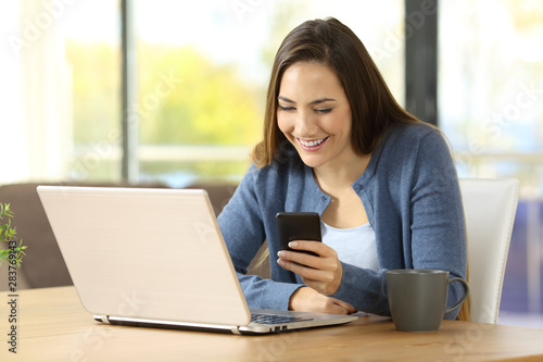 Happy woman uses phone and laptop at home