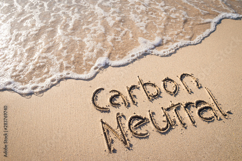 Carbon Neutral message handwritten on smooth sand beach with incoming wave