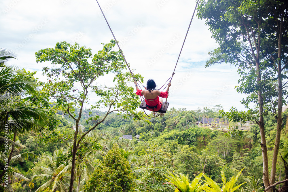 Young tourist woman swinging over the tropical rainforest at Bali island