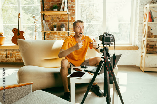 Young caucasian male blogger with professional camera recording video review of gadgets at home. Blogging, videoblog, vlogging. Man making vlog or live stream about photo or technical novelty. photo