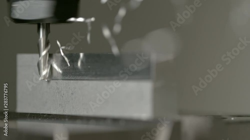 SLOW MOTION, MACRO, DOF: Twisted pieces of excess metal fly off a piece of aluminium during lathing by a CNC drill. Fine cut end mill shaving the side of a matt block of metal. Micro machining process photo
