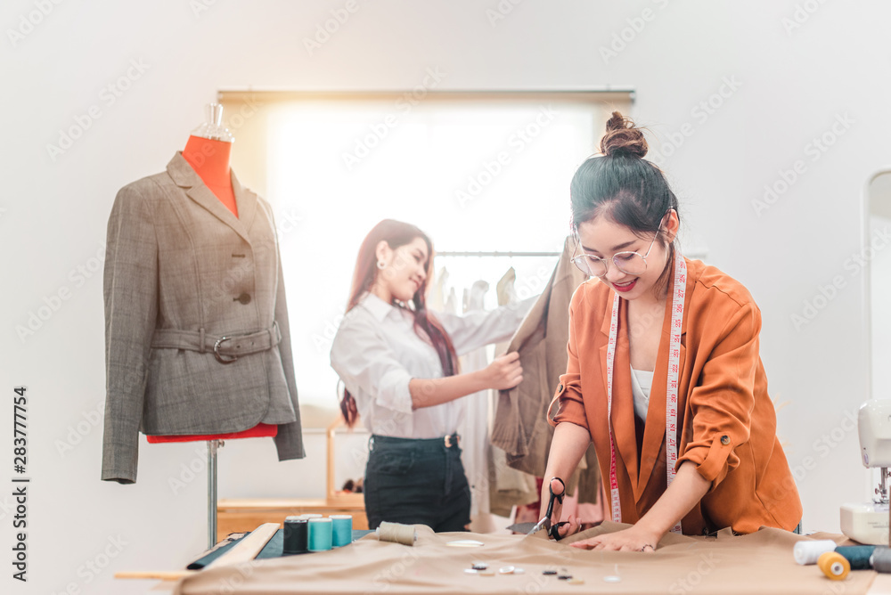 Young dressmaker woman sews clothes on sewing machine. Smiling seamstress and her hand close up in workshop. Focus on sewing machine and tissue. Young dressmaker woman sews clothes on sewing machine. Smiling seamstress and her hand close up in workshop. Focus on sewing machine and tissue.