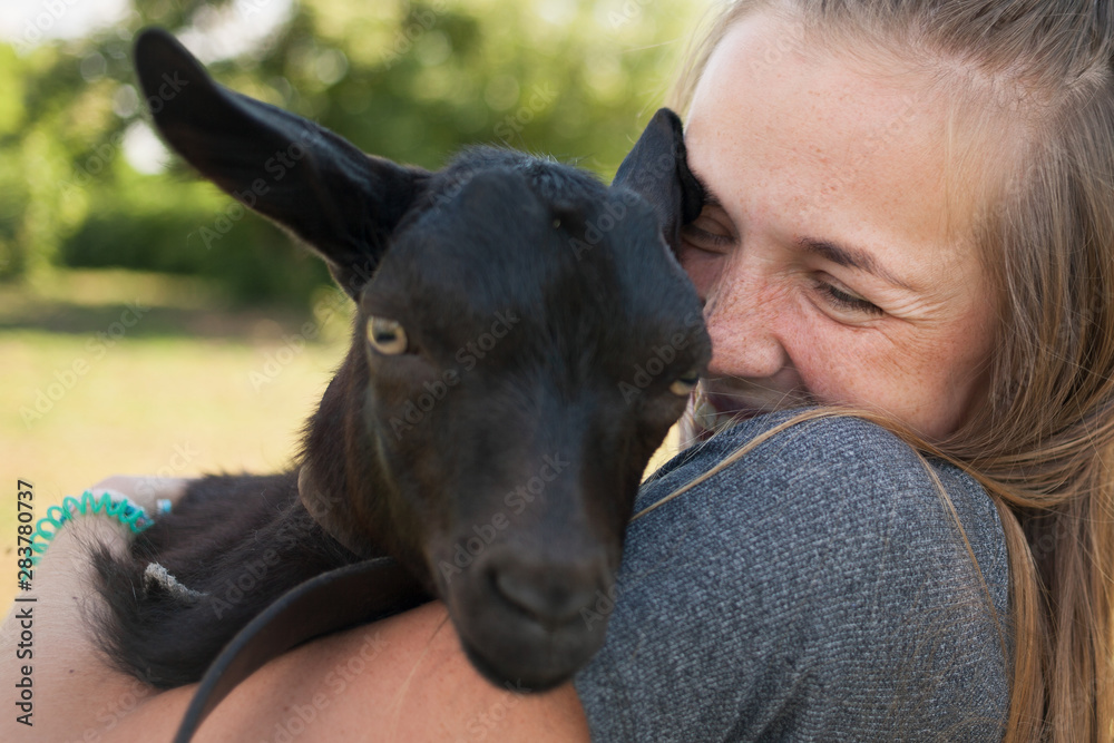 Contact zoo. Young smiling girl holding a black goat in her arms. Contact zoo. Young smiling girl holding a black goat in her arms.