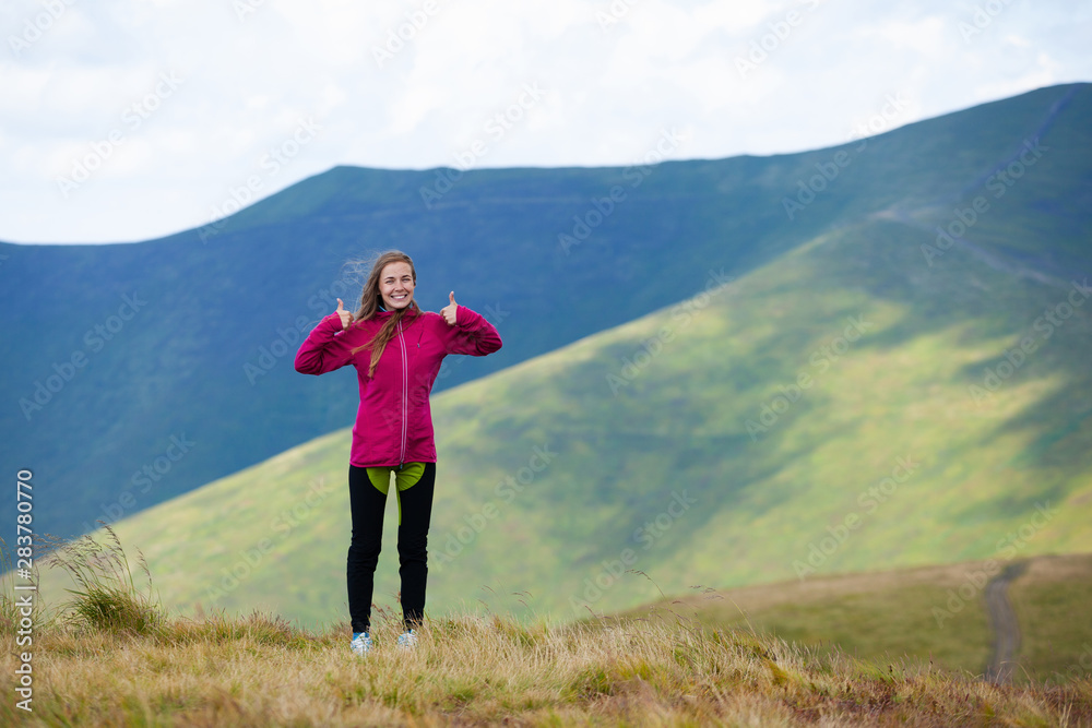 Young smiling traveling girl standing on a hill showing thumbs up