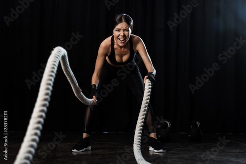 Fototapeta Naklejka Na Ścianę i Meble -  selective focus of sportswoman exercising with battle ropes on black