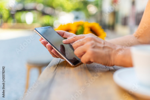 Happy female using smartphone at modern coffee shop, she chatting Online Messaging on mobile. Hand of woman using smartphone on wooden table, Space for text or design.